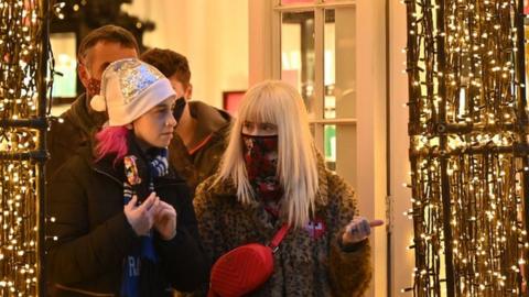 Shoppers wearing face coverings to combat the spread of Covid-19, leave through the decorations adorning a doorway of a store in central London on December 21, 2021