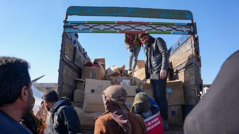 Syrians receive aid at a makeshift shelter near the rebel-held town of Jinidayris