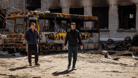 Men walk near a burnt bus and a damaged school in Bohdanivka village
