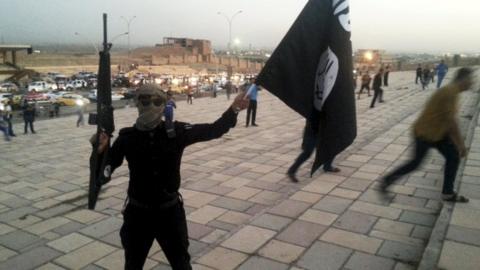IS fighter holds a flag of the group and a weapon on a street in Mosul