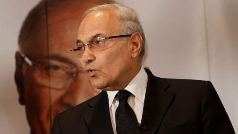 Ahmed Shafiq, pictured in a dark suit and tie in front of a large photo of his own face, in a 2012 photo