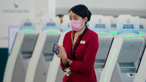 A Cathay Pacific staff member wearing a facemask next to a row of self-check in terminals in Hong Kong.