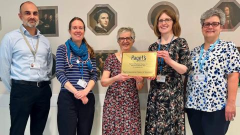 Image of Paget’s Association Trustee Amanda Sherwood (centre) presenting the Centre of Excellence plaque to RNHRD staff.