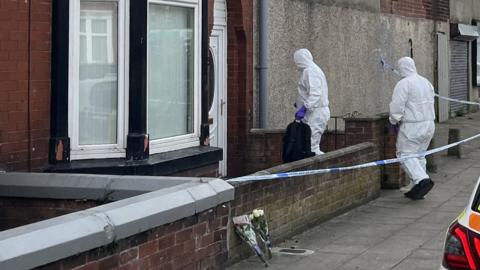Two people in white forensic suits enter a house