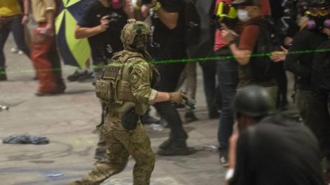 A federal officer with a handheld device attempts to disperse a large crowd 20, July 2020