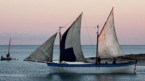 A schooner sails from the coast at dusk