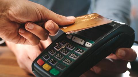 Stock image of a hand holding a credit card, paying using a contactless card reader