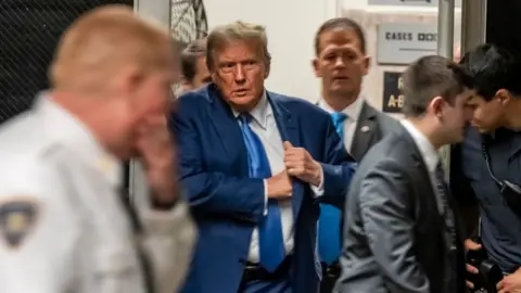 Donald Trump exiting court, getting something out of his jacket pocket.