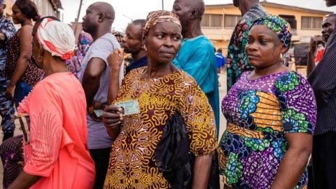 A voter holds her her voter card while queueing with others at a polling at Agege, Lagos on February 25, 2023, during Nigeria's presidential and general election