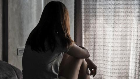 A woman sits on a bed with her back to the camera