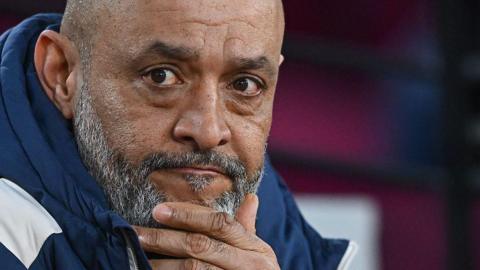 Close-up of Nuno Espirito Santo. He has a greying beard and is wearing a navy coat. He is resting one of his hands against his chin.