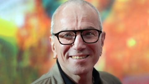 Daniel Day-Lewis wearing glasses in front of a bright orange and green background