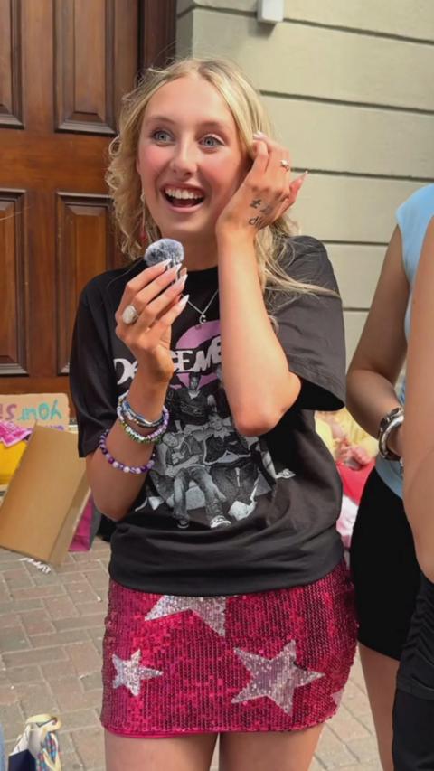 A blonde haired woman in black tshirt and a pink sparkly skirt with stars on it.