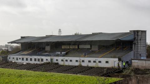 A dilapidated stand with grass in front of it 