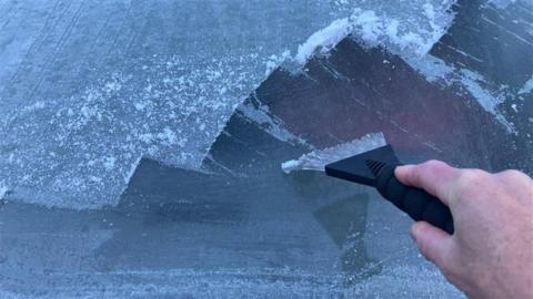 Man scraping ice off car windscreen