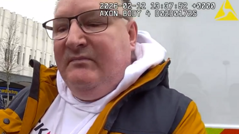 Man in yellow and black puffer jacket with large face and glasses.