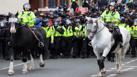 Police officers on police horses with police officers in front of a crowd of protesters in Bolton