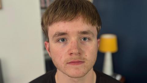 Judah Cousin looks into the camera. He has brown hair and he's wearing a black t-shirt. It is a head and shoulders shot of him. 