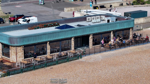 An aerial image of the cafe on Hove seafront. The roof is blue. There is seating on a terrace on the beach. 