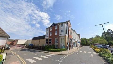 A Google photo of a Travelodge hotel with three floors next to a car park. No cars or people can be seen.