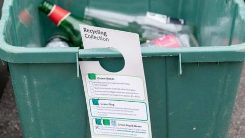 Information tag hangs from green box with glass bottles inside
