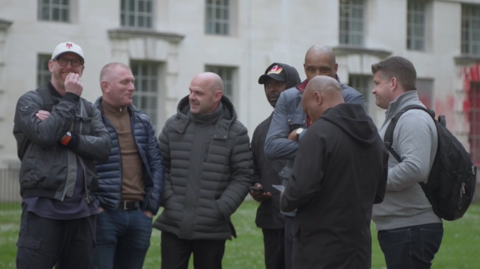 Footballers, including Tommy Johnson, Danny Murphy, Andy Cole and Brian Deane, stand together talking in Westminster. 