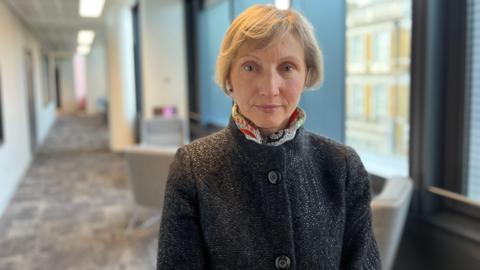 Marina Litvinenko. She has short blonde hair and is wearing a dark grey coat with a colourful, patterned scarf around her neck. She is looking directly at the camera and smiling. 