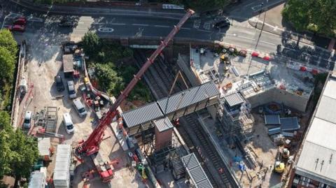 An aerial shot of a large crane placing a footbridge above a train track