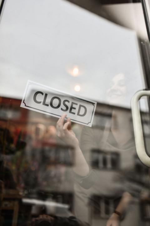 A woman flipping a closed sign over on a glaring glass door