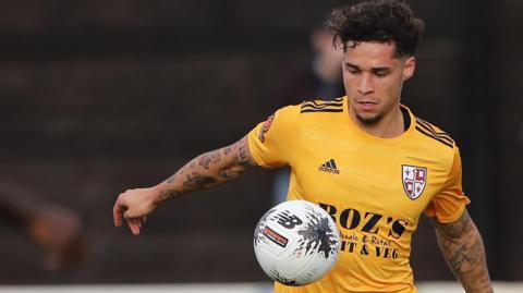 Lewis Walker controls the ball on his chest during a game for Woking. He is wearing a yellow shirt.