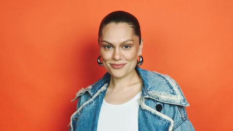 Jessie J with her hair tied back, big silver hoop earrings and a denim jacket and white top