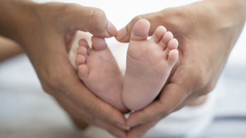 woman's hands cupping a baby's feet, producing a heart shape
