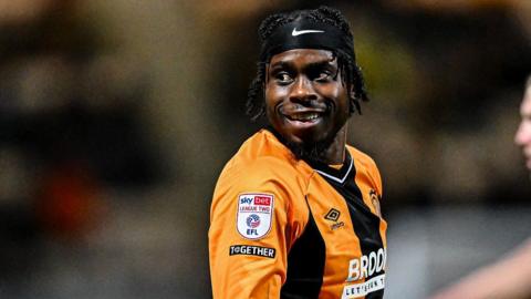 Cambridge United's Pelly Ruddock Mpanzu smiling over shoulder wearing home kit