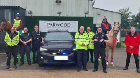 Officers stand around a car, with two horse riders at the side of the image and a sign which reads "parwood equestrian centre"