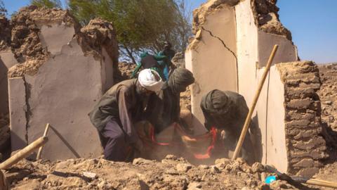 Afghan men comb through the rubble to collect belongings and recover bodies in the aftermath of a devastating 6.3 magnitude earthquake in Herat