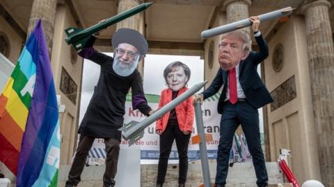 Anti-war activists hold mock nuclear missiles and wear masks of (L-R) Iranian Supreme Leader Ayatollah Ali Khamenei, German Chancellor Angela Merkel and US President Donald J. Trump as they perform in front of the Brandenburg Gate in Berlin,
