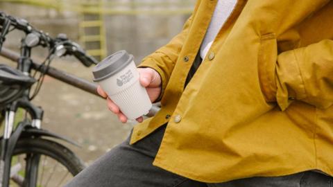 A man in a yellow jacket holding a reusable cup