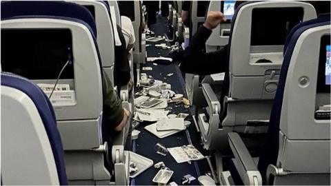 Aftermath of turbulence shows trash and food on plane floor.