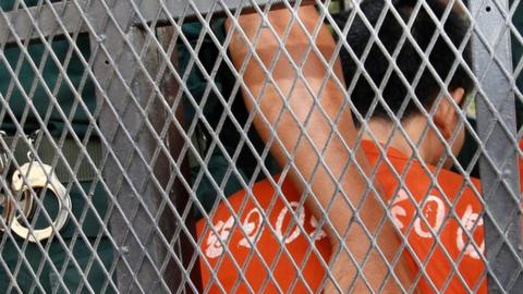 Cambodian Oeuth Ang, in prison uniform and facing away from the camera, behind the a police van wire mesh, outside court in Phnom Penh, Cambodia, 23 March 2017.