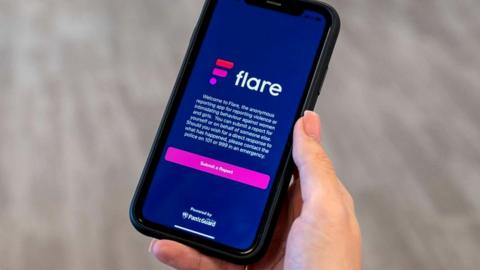 Woman holding a phone showing the Flare Report app on screen