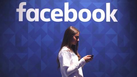 Youn woman checking phone under facebook logo