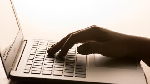 A hand resting on top of keyboard on a laptop. The background is white.