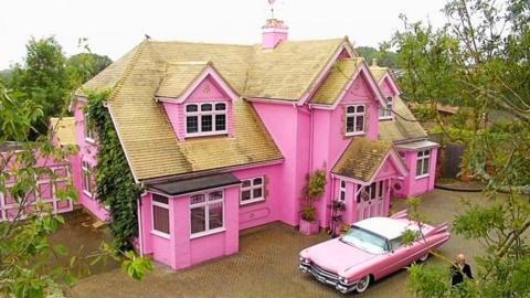Huge pink house with pink cadillac parked in front