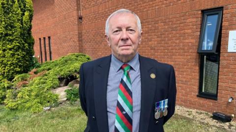 Tom Herring with short white hair wearing a dark jacket on which three medals are pinned