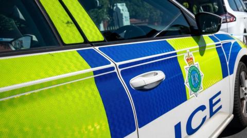 A police car is parked on a street. A sticker on the front door reads 'Merseyside Police'. 