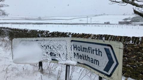 Holmfirth road sign next to snow covered field