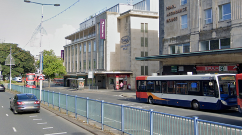 Google image of Courtenay Street in Plymouth. Buses and cars are using the road. A barrier is separating the two carriages. A Premier Inn building is situated on the side of the road.