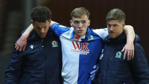 Hayden Carter is helped off the field by two members of the Blackburn coaching staff