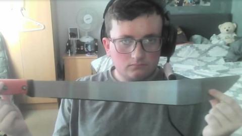 Jacob Graham in his bedroom holding up a machete