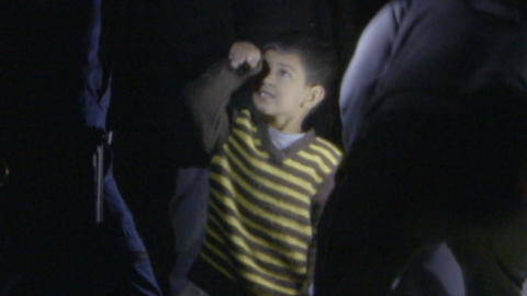 A child in a striped top is surrounded on all sides by uniformed police that he is only waist-high to in this night-time photograph